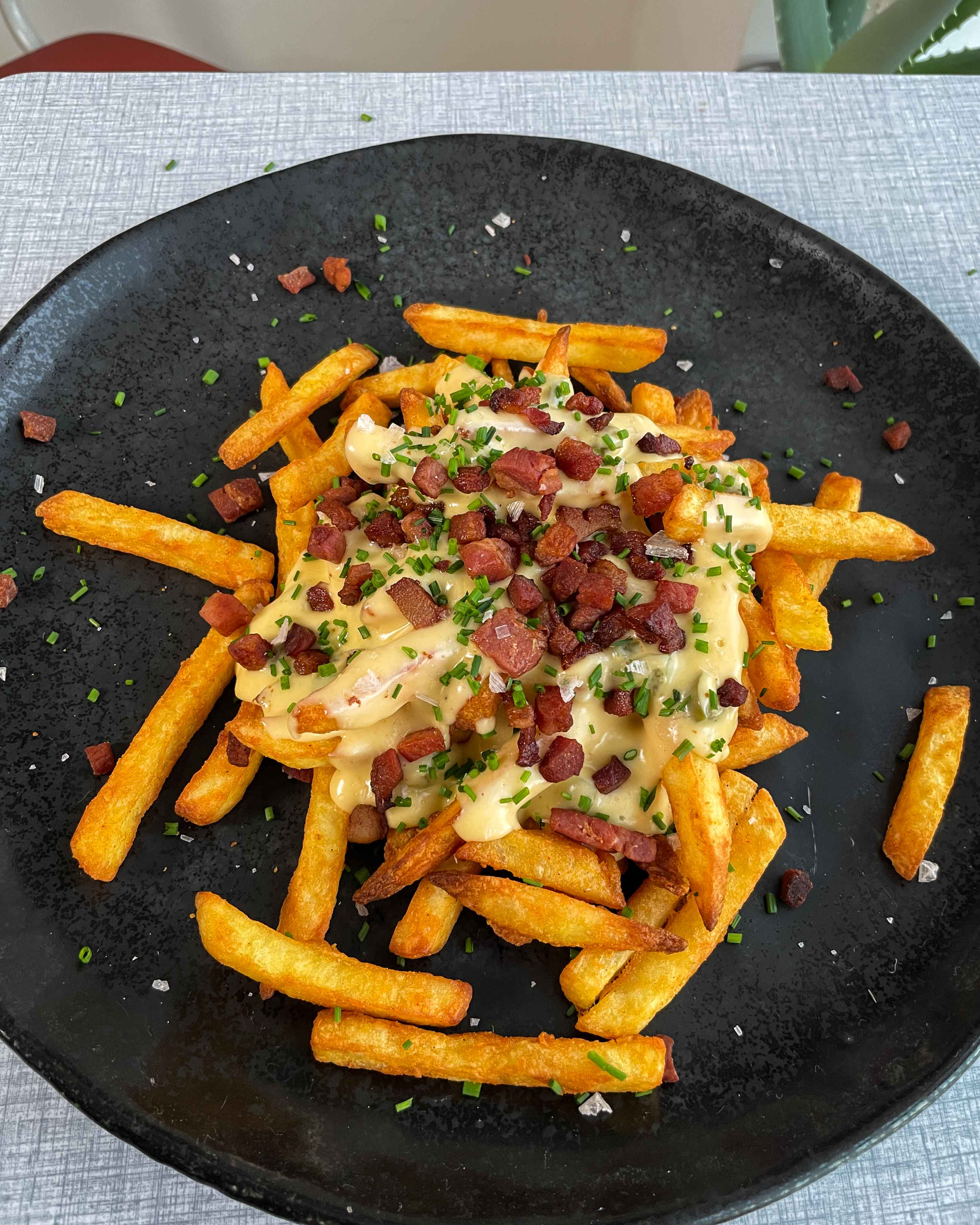 En appetitvækkende tallerken fyldt med lækre chili cheese fries: Sprøde gyldne fritter toppet med krydret ostesovs og knasende bacon.