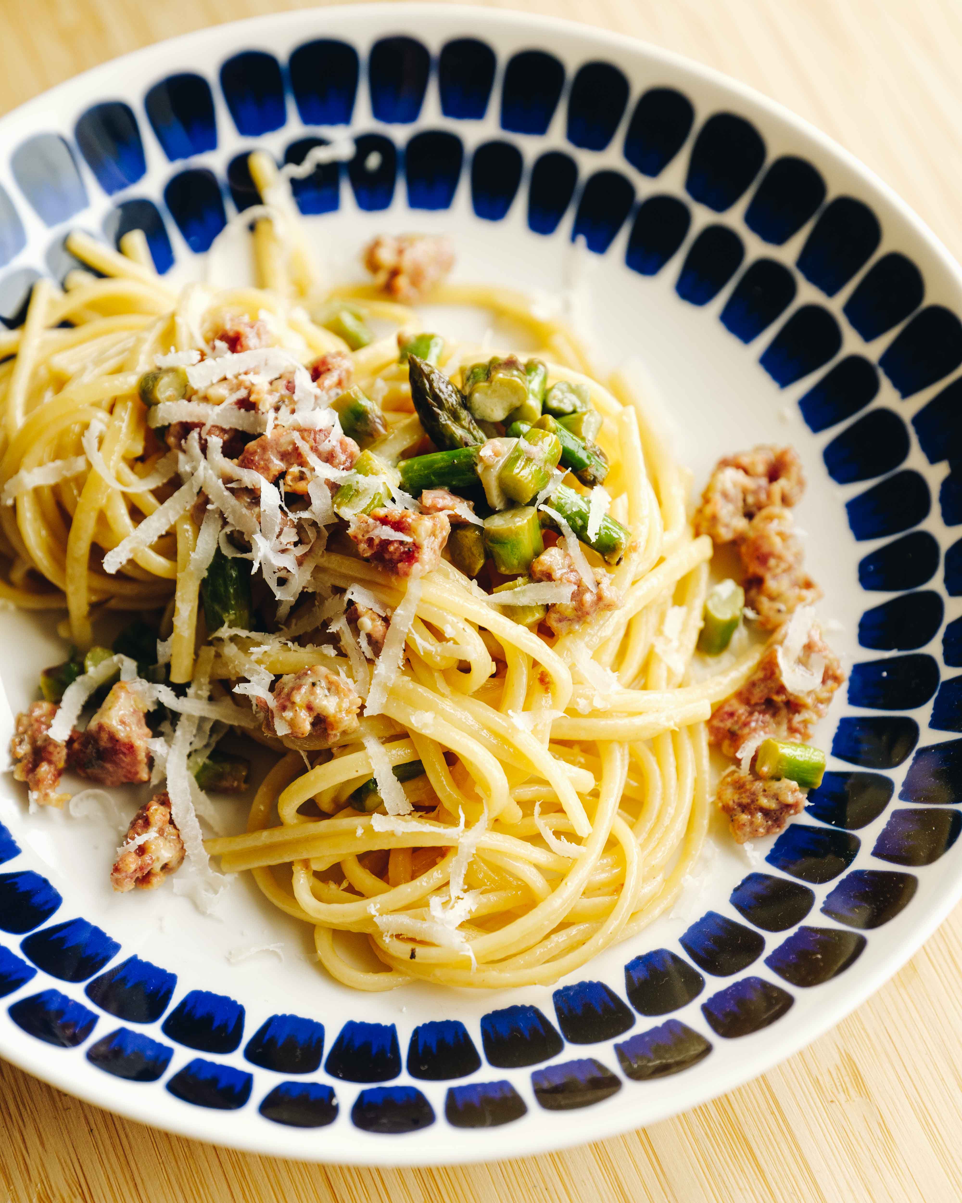 Cremet pasta med salsiccia, grønne asparges og friskrevet parmesan i en lys skål på træbord.