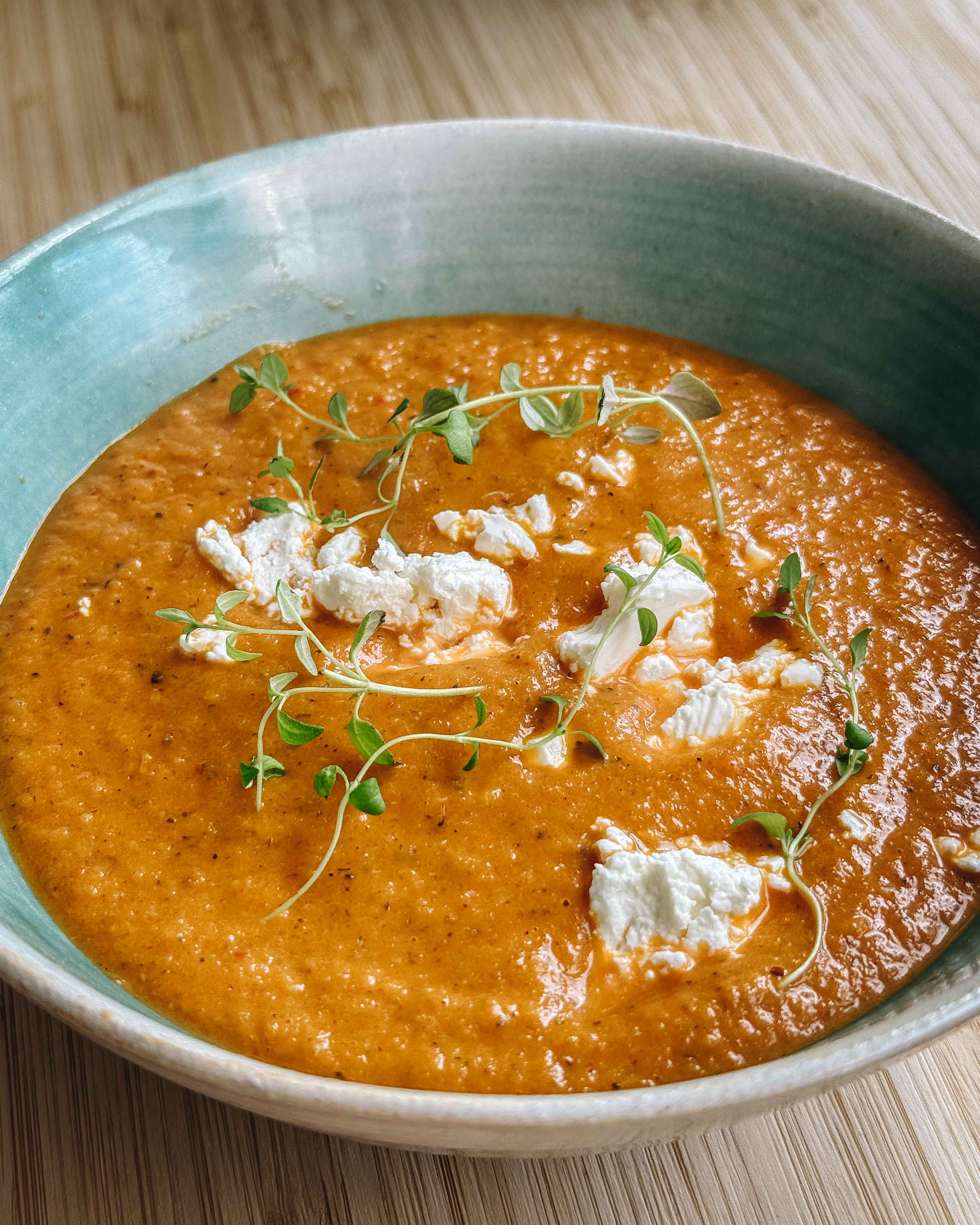 Cremet grøntsagssuppe serveret med feta og frisk timian i en dyb tallerken på et rustikt bord.
