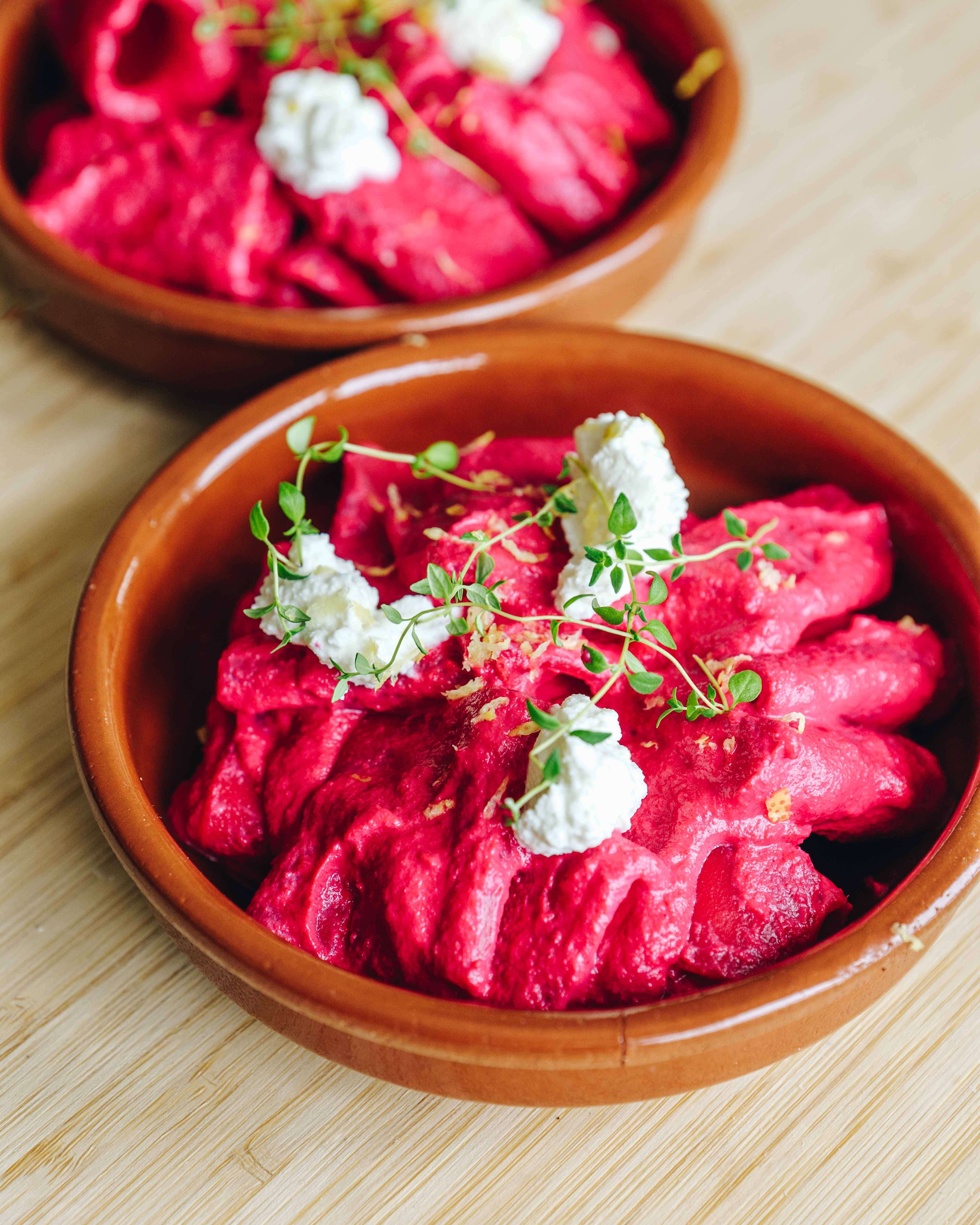 Pink pasta med cremet rødbedesovs, toppet med ricotta, frisk timian og citronskal på en lys tallerken.