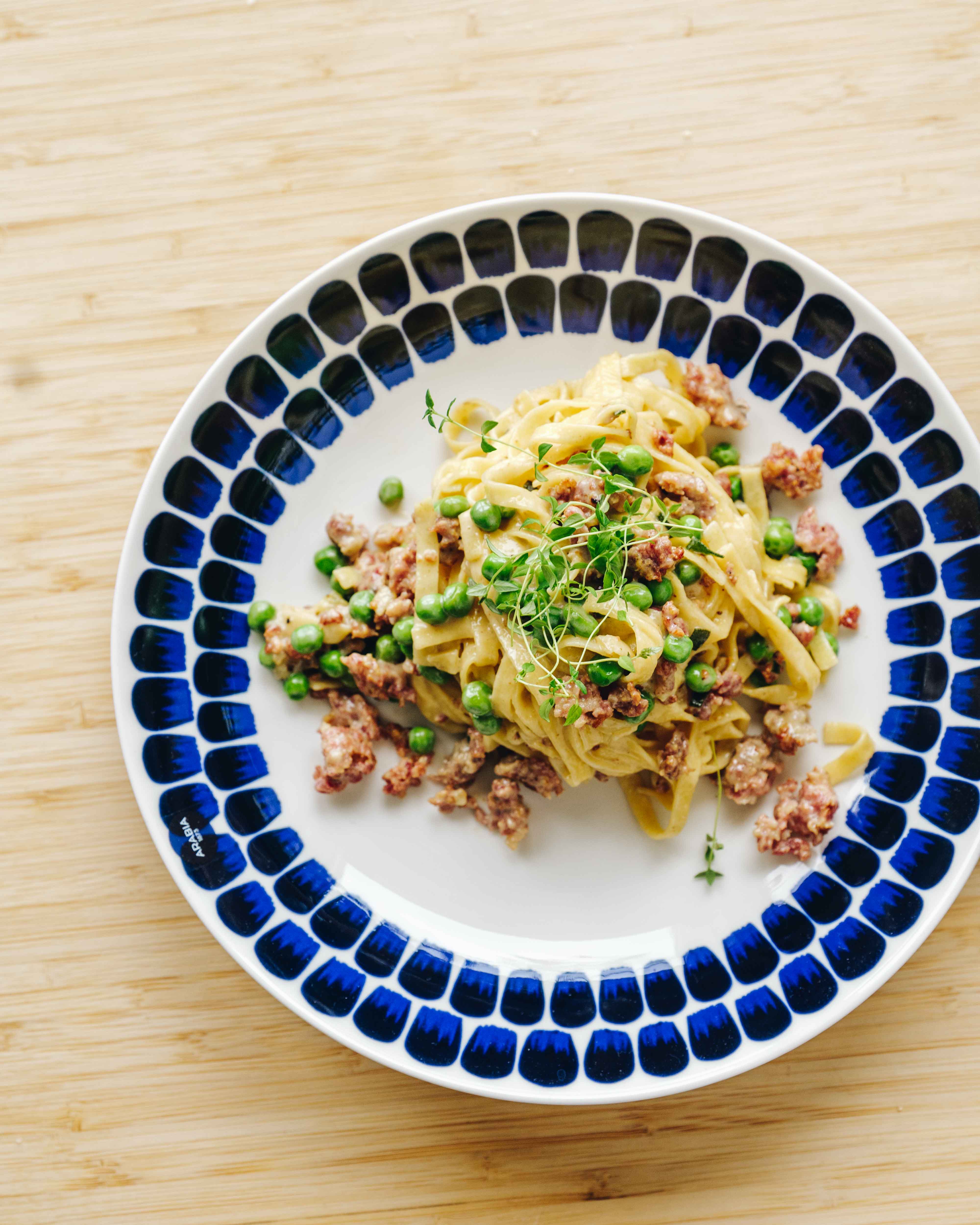 Skål med cremet pasta med salsiccia, ærter og parmesan, toppet med frisk timian.