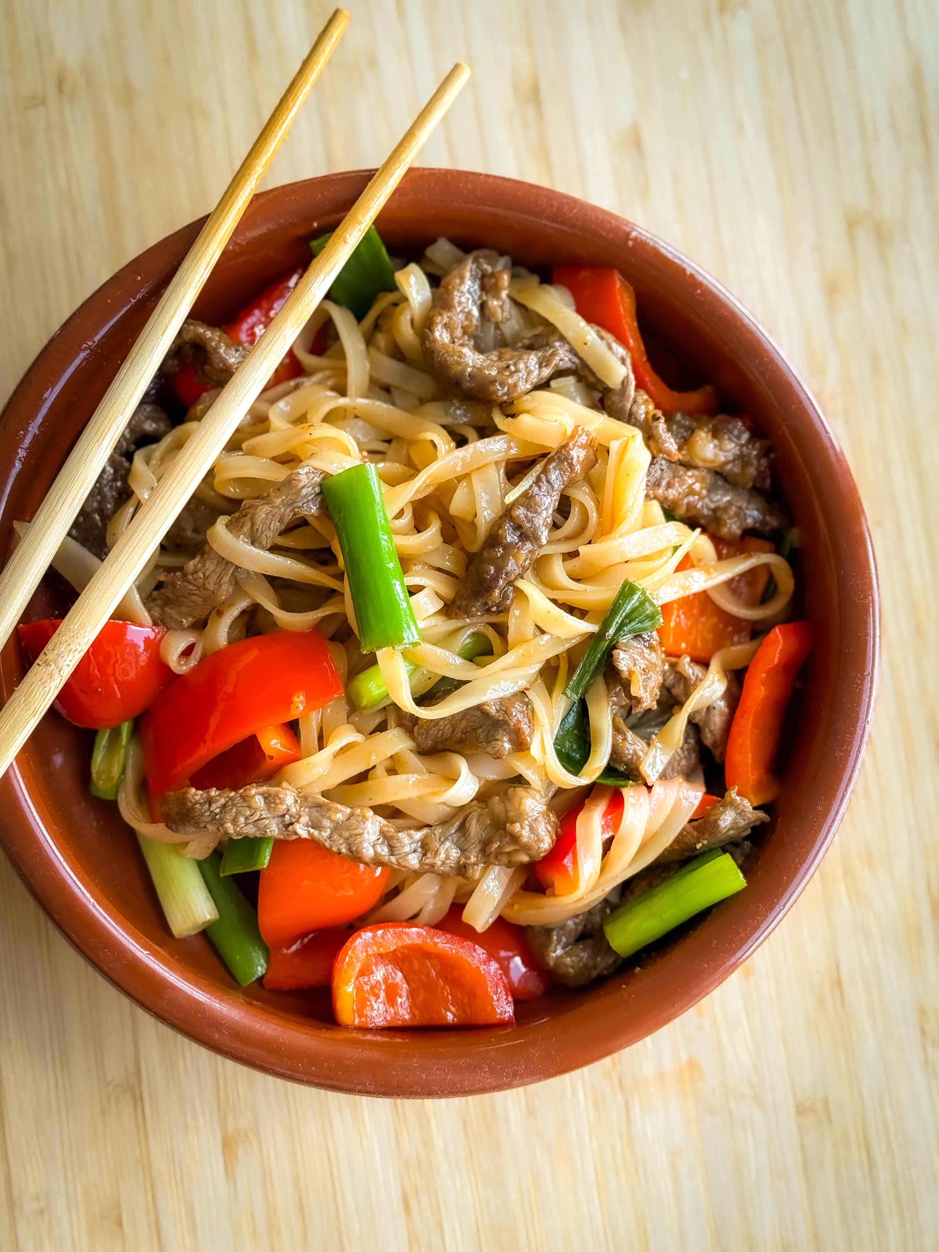 En skål med beef stir fry med risnudler, rød peberfrugt og forårsløg