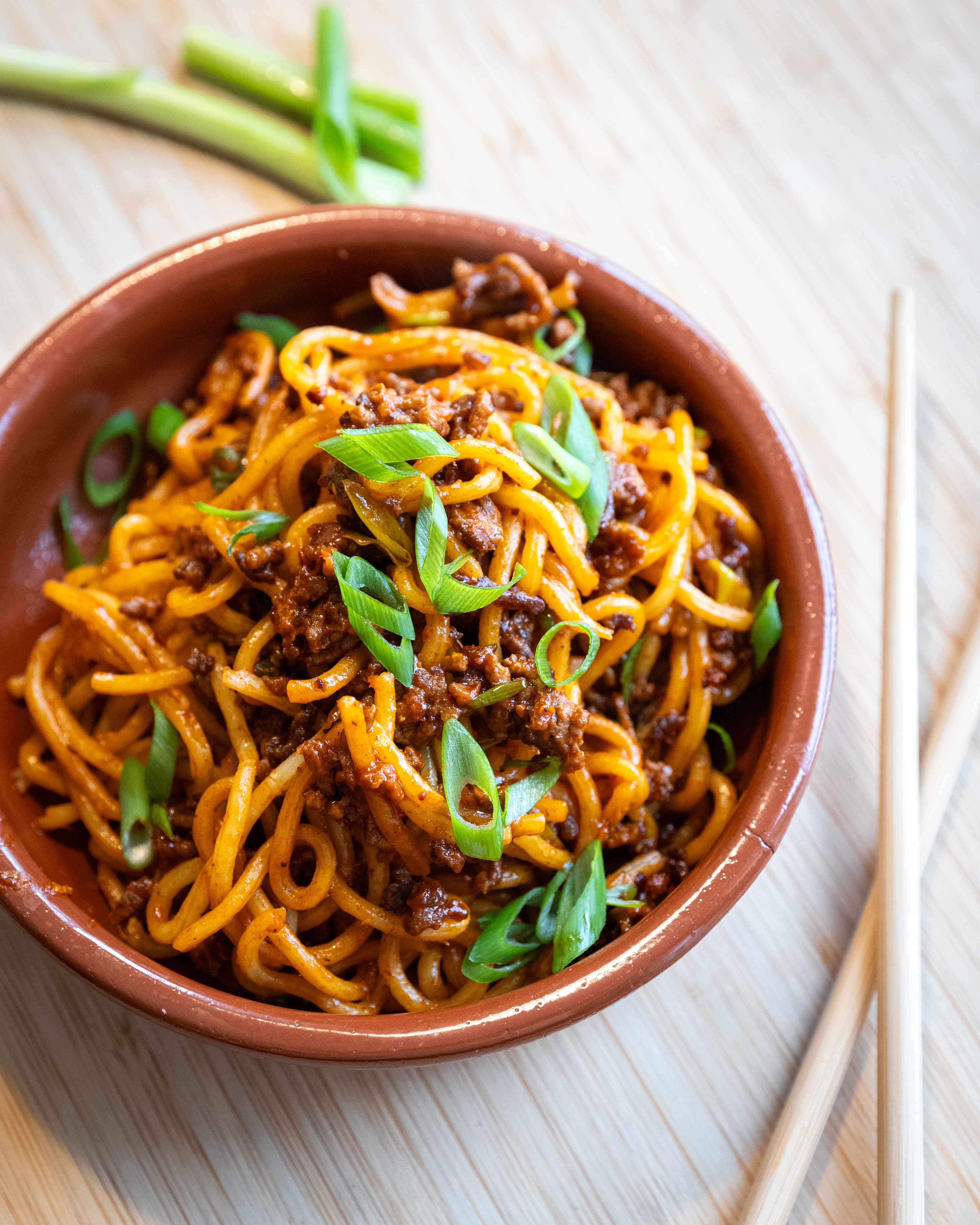 Skål med gochujang nudler med oksekød, toppet med forårsløg og blank, krydret sauce.