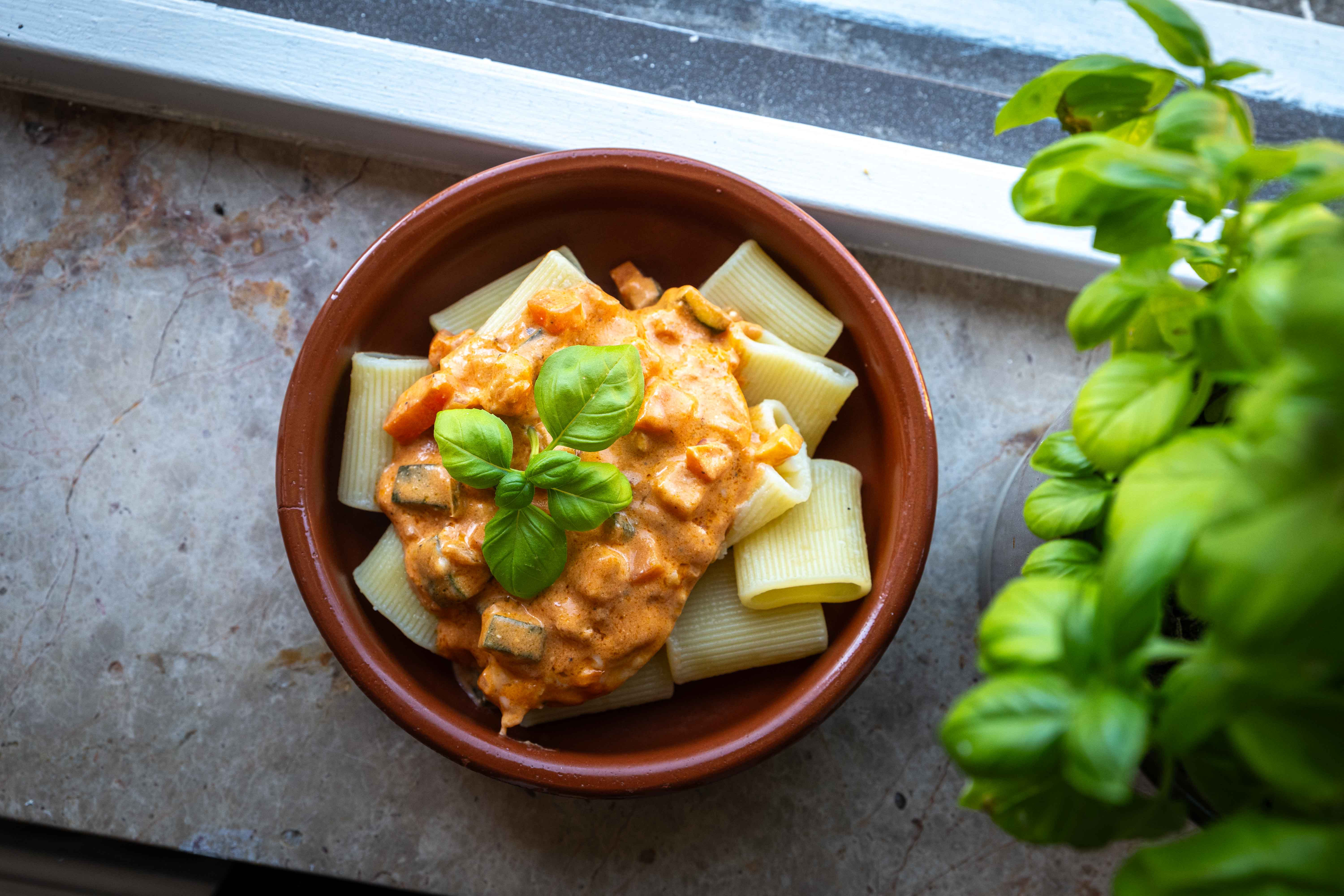 Kylling i cremet tomatsovs med pasta og grøntsager serveret i en dyb tallerken med revet parmesan på toppen.