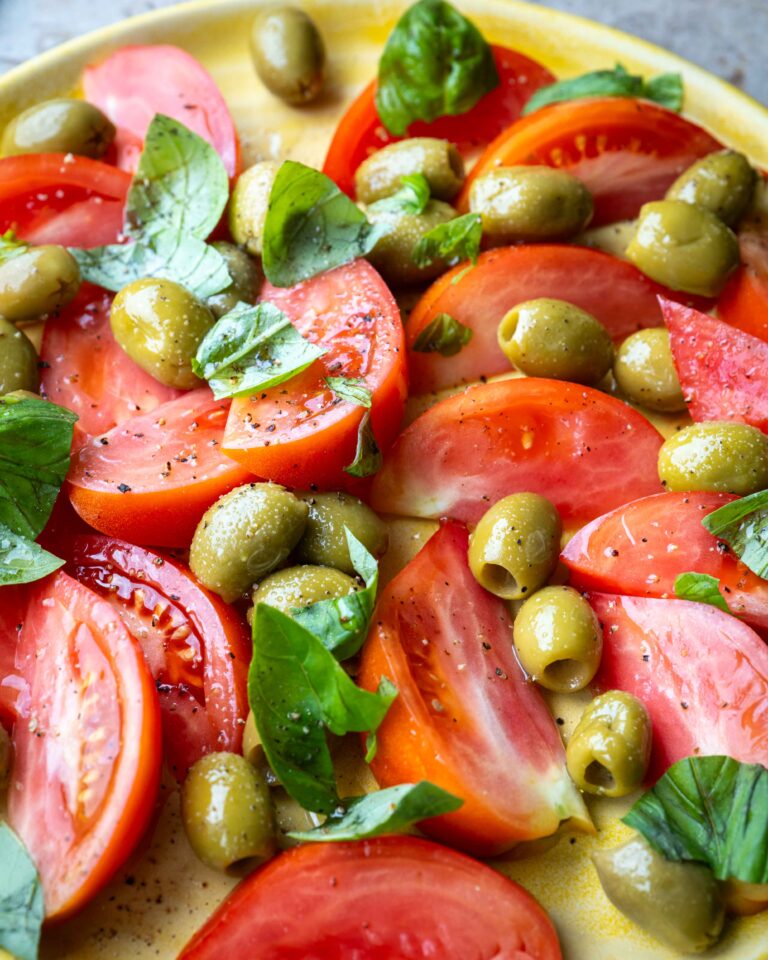 Nem tomatsalat med grønne oliven, frisk basilikum og olivenolie på en tallerken