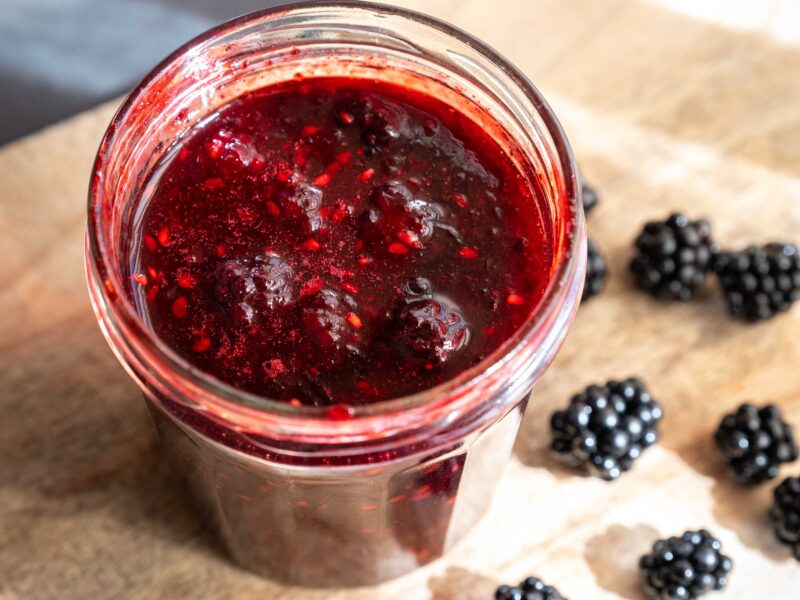 Hjemmelavet brombærmarmelade med kardemomme i et lille glas med friske brombær ved siden af